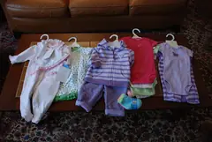 Бебешки дрехи на закачалки, подредени върху маса